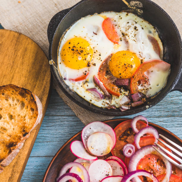 istock Rustic breakfast in a family hotel - scrambled eggs with vegetables in a cast-iron pan and fresh salad with radish, tomatoes and red onion rings in a plate, top view, close-up 1190625133