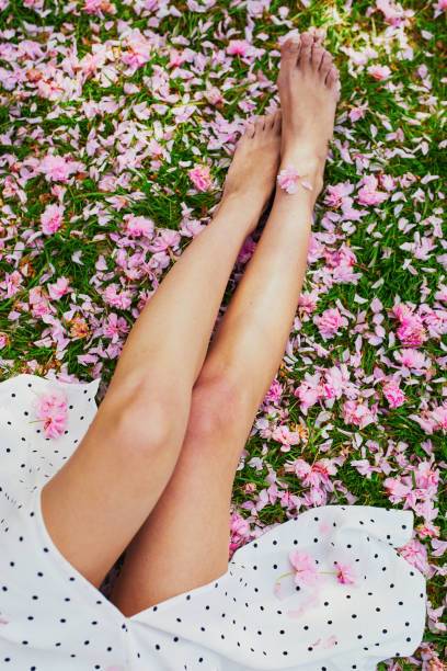 frau sitzt auf dem gras mit rosa kirschbaum blütenblätter und blumen bedeckt - vertical single flower women teenager stock-fotos und bilder