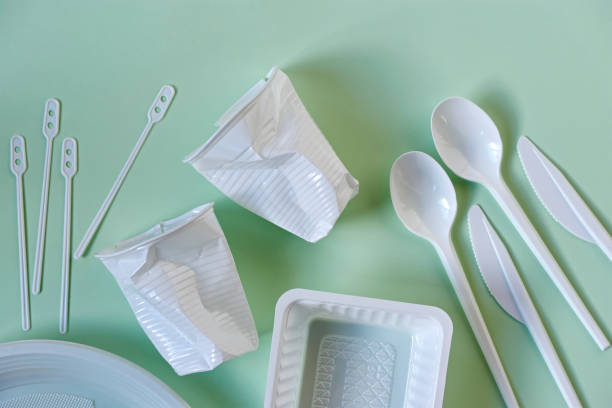 Plastic cups, spoons, knives, stirrers, plate and box on green Two smashed white plastic coffee cups, spoons, knives, stirrers, plate and box on a light green background. Zero waste, plastic free, stop pollution, ecological concept. disposable photos stock pictures, royalty-free photos & images