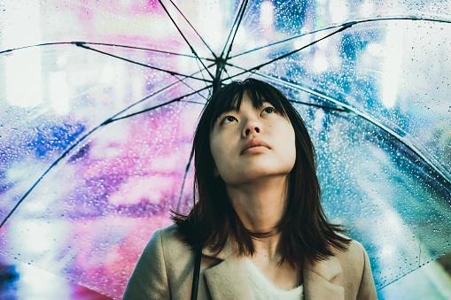 Asian young woman is having an umbrella under the rain in the night.