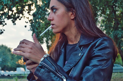Beautiful girl in black rocker leather jacket lighting up a cigarette