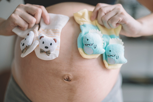 primer plano en asiático chino embarazada señora sosteniendo 2 pares de botines de bebé en frente de su vientre que espera bebés gemelos entrega photo