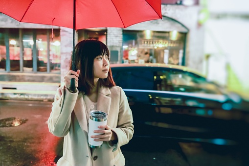 Asian young woman is having an umbrella under the rain in the night.