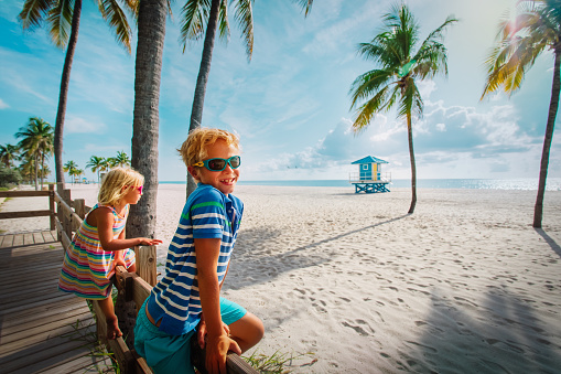 happy boy and girl looking at tropical beach with palms, family vacation at sea