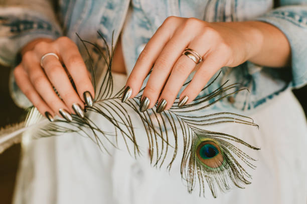 Stylish trendy female mirror manicure, metal nail art, holding peacock feather stock photo