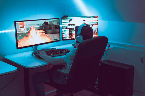 Boy plays video game online and sits in front of two big computer monitors Boy sits in front of two monitors connected to a desktop gaming computer. He plays video games at night and he wears a headset, which enables him to communicate with other online players. The game on screen is an action game with guns and explosions. 
Note: Both images on the screens are my work. Property releases attached. motion picture screen stock pictures, royalty-free photos & images