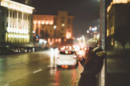 Woman at the street during winter texting for taxi through mobile app