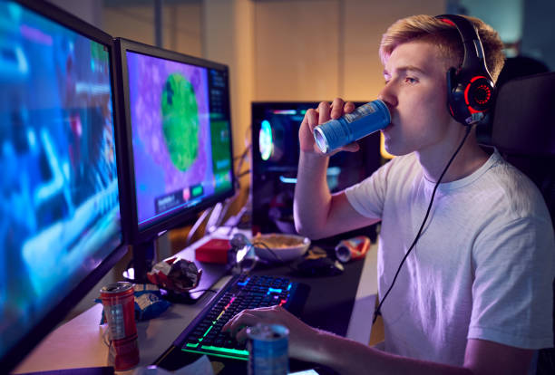 o adolescente que bebe o jogo da bebida da energia da cafeína em casa usando telas de computador duplas na noite - molécula de cafeína - fotografias e filmes do acervo