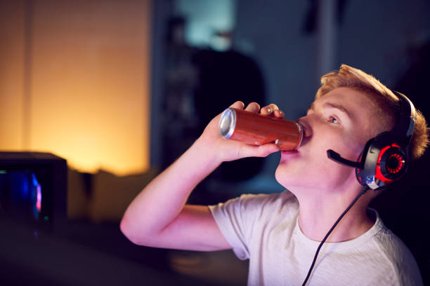 Teenage Boy Drinking Caffeine Energy Drink Gaming At Home Using Dual Computer Screens At Night Teenage Boy Drinking Caffeine Energy Drink Gaming At Home Using Dual Computer Screens At Night energy drink stock pictures, royalty-free photos & images