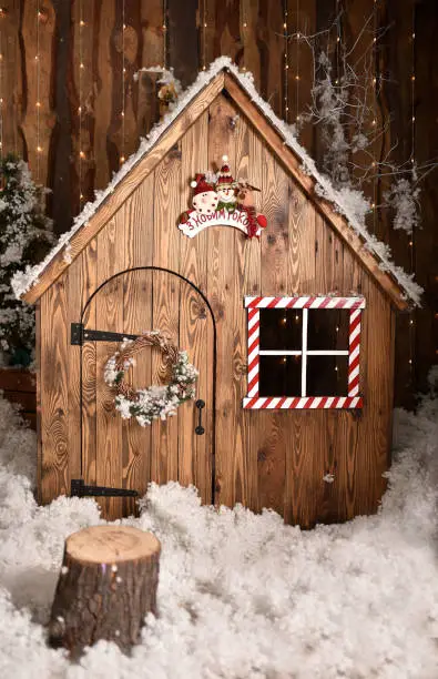 Fairytale house decorated for winter holidays season covered by fresh snow glowing in the dark during Christmas eve. Log wood fence and draw-well on a front yard. Christmas and New Year outdoor decor.