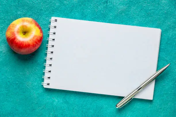 blank spiral sketchbook with an apple and pen against turquoise handmade textured paper