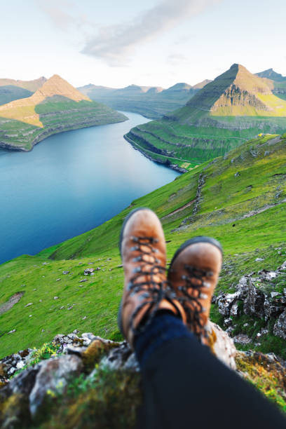 Boots of lonely tourist over majestic fjords of Funningur Boots of lonely tourist over majestic fjords of Funningur, Eysturoy island, Faroe Islands. Landscape photography eysturoy stock pictures, royalty-free photos & images