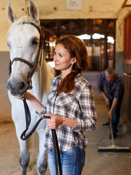 istock Farmer standing with horse, man cleaning floor at stabling 1190669561