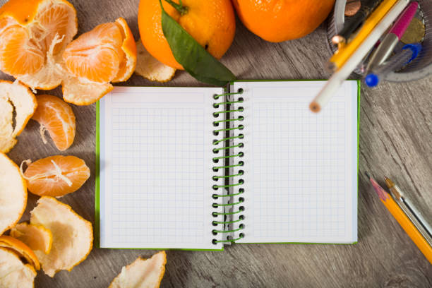 Detailed notebook with writing utensils surrounded by mandarins