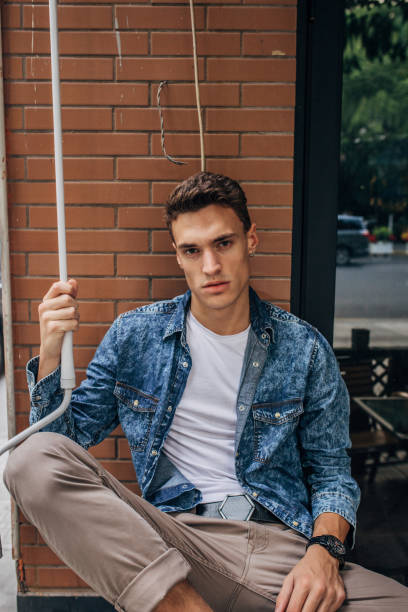 Portrait of a young LGBTQ+ stylish man sitting on a doorstep in the street