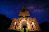 night bell tower ruin in forest at starry night and man with flashlight under it