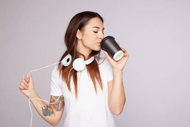 красивая женщина пьет кофе, слушая музыку в наушниках. - headphones women tattoo music стоковые фото и изображения