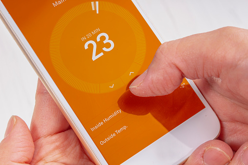 Woman holding a smart phone changing the room temperature thermostat