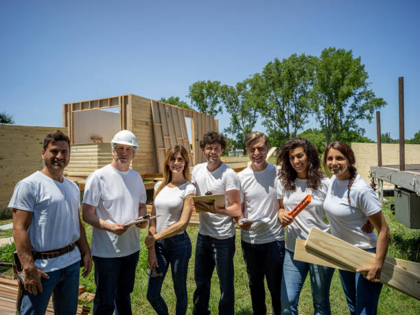 istock Happy group of volunteers at a construction site facing camera smiling while holding tools, plywood and clipboards 1190692003