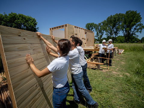 Latin american volunteers lifting up a wall at a charity construction project while leaders discuss something at background