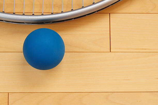 A blue rubber racquetball and racquet on a wooden floor Blue Rubber Racquetball and Racquet on Hardwood Court Floor racketball stock pictures, royalty-free photos & images