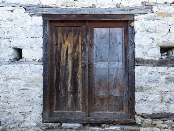 Weathered wooden door with wood beams between layers of stone in an old building.