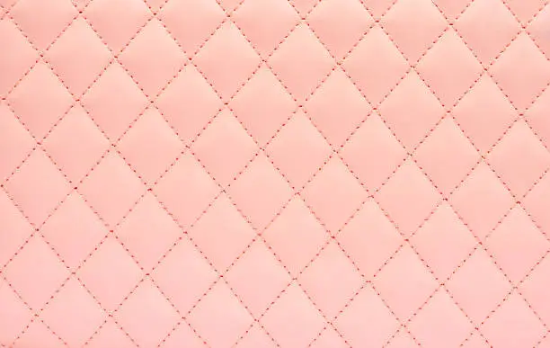 Photo of Natural leather background colored in pink and sewn in the form of rhombus.