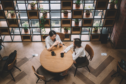 top angle of 2 office white collar female worker taking a coffee break at the office cafeteria having discussion