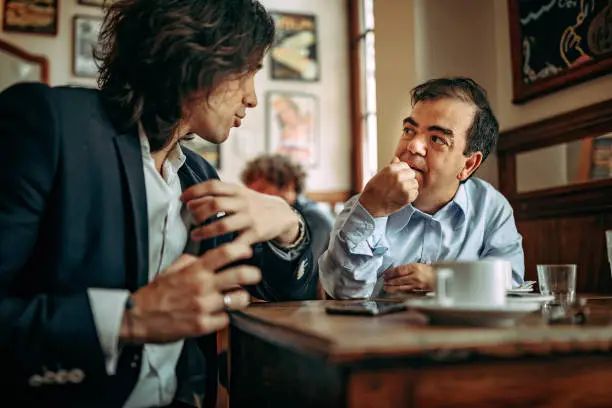Businessman discussing with dwarfish colleague at coffee shop