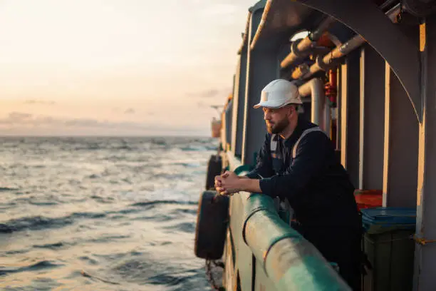 Marine Deck Officer or Chief mate on deck of offshore vessel or ship , wearing PPE personal protective equipment - helmet, coverall. He holds VHF walkie-talkie radio in hands.