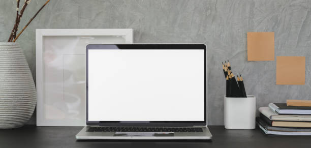 istock Modern workplace with open blank screen laptop computer and office supplies on black table and grey wall 1190769910
