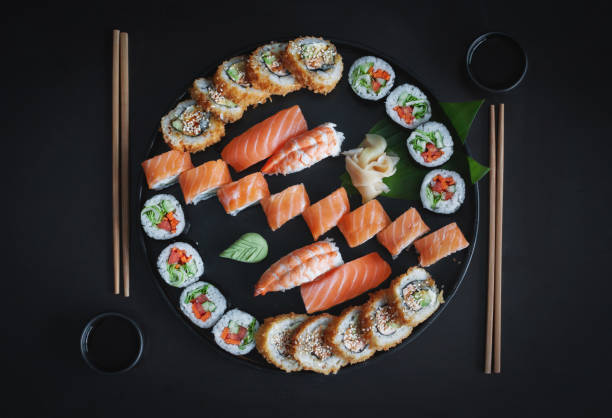 cuisine japonaise. ensemble avec sushi nigiri classique, fusion uramaki chaud, philadelphie et unagi rouleaux à partir d'ingrédients frais sur une assiette ronde en bois à fond noir. vue du haut, copier l'espace. - maki sushi photos et images de collection