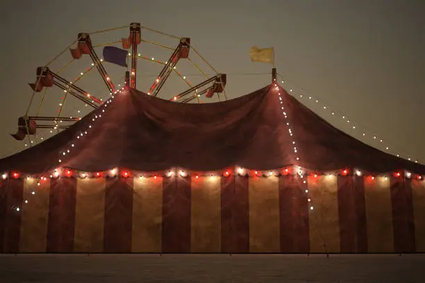 Beautiful night time carnival image of a big top tent and a ferris wheel in the background.