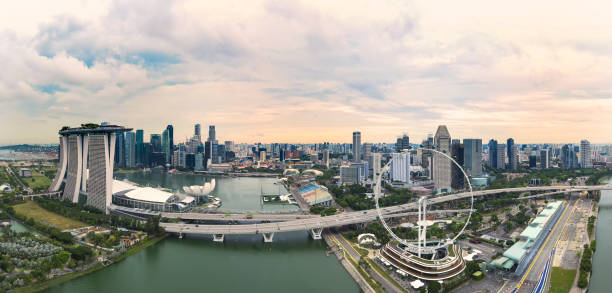 上空からの眺めは、遠くに金融街とフォアグラウンドのフェリーホイールと劇的な夕日の間にシンガポールのスカイラインの素晴らしい空中写真。 - marina bay sands hotel architecture asia travel destinations ストックフォトと画像