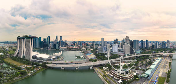 vista de cima, vista aérea impressionante da skyline de singapore durante um por do sol dramático com o distrito financeiro na distância e em uma roda da balsa no primeiro plano. - singapore skyline - fotografias e filmes do acervo