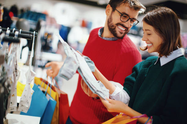 New year will start with another family member. Young couple Christmas shopping together. They are standing and choosing baby clothes for their baby child that they expect soon. cute pregnant woman with gift stock pictures, royalty-free photos & images