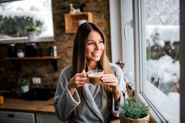 istock Beautiful smiling brunette looking through window and drinking coffee in the kitchen. 1190798246