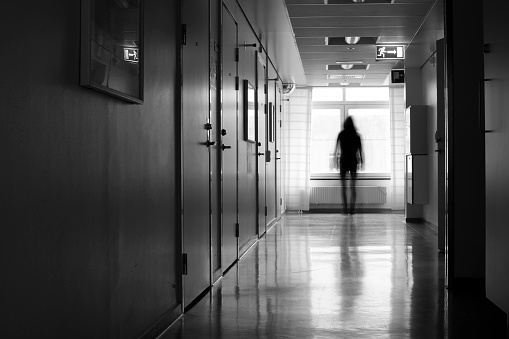 Unrecognizable silhouette of person in blurred motion in front of window in a hostpital corridor.