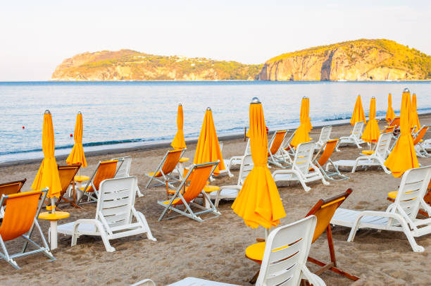 istock White plastic and metal construction with yellow fabric deckchairs together with yellow umbrellas on the sand beach of Tyrrhenian sea with mountains on background in Italy 1190805468