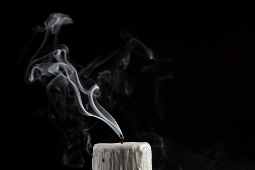 Smoke emitting from burnout candle against black background.