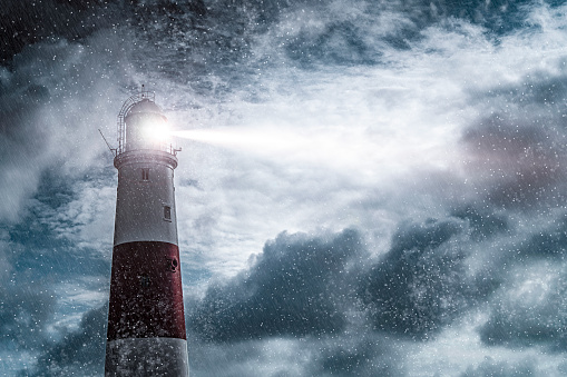 Large red and white lighthouse on a rain and storm filled night with a beam of light shining out to sea