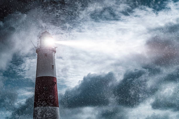 Large lighthouse with bright search light on a dark and stormy night Large red and white lighthouse on a rain and storm filled night with a beam of light shining out to sea searchlight photos stock pictures, royalty-free photos & images