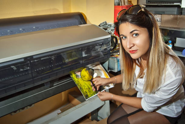 la ragazza con una camicia bianca stampa una foto. donna che guarda attraverso la foto con lente d'ingrandimento. l'assistente controlla l'immagine stampata. natura, verde e tenda nella foto. - photobusiness foto e immagini stock