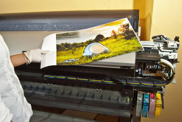 the girl in a white shirt prints a photo. woman looking through photo with magnifier. the assistant checks the printed image. nature, greenery and tent in the photo. - photobusiness imagens e fotografias de stock