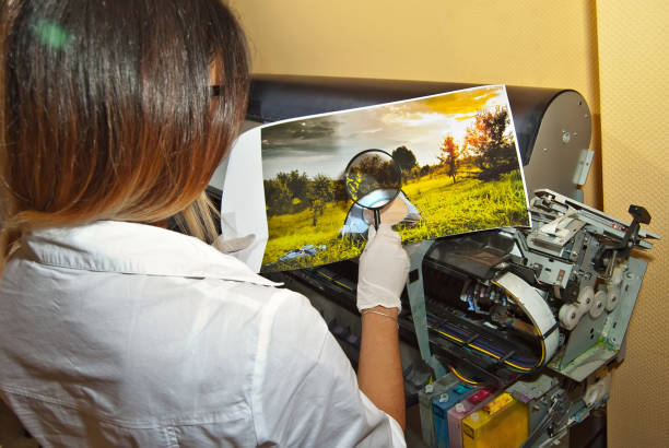 la ragazza con una camicia bianca stampa una foto. donna che guarda attraverso la foto con lente d'ingrandimento. l'assistente controlla l'immagine stampata. natura, verde e tenda nella foto. - photobusiness foto e immagini stock