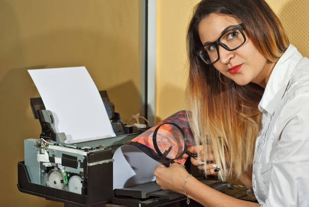 the girl in a white shirt prints a photo. woman looking through photo with magnifier. the glasses assistant checks the printed image. sunset in the photo. - photobusiness imagens e fotografias de stock