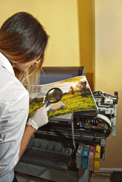 the girl in a white shirt prints a photo. woman looking through photo with magnifier. the assistant checks the printed image. nature, greenery and tent in the photo. - photobusiness imagens e fotografias de stock