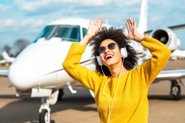 hermosa chica lanzando sus manos en el aire escuchando música edificante frente a un cono nasal de un avión privado estacionado en una pista de rodaje del aeropuerto - status symbol audio fotografías e imágenes de stock