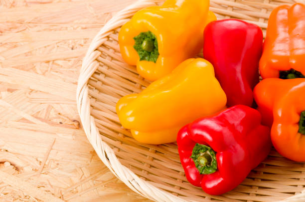fresh Colored bell pepper on bamboo colander on OSB plywood board background
