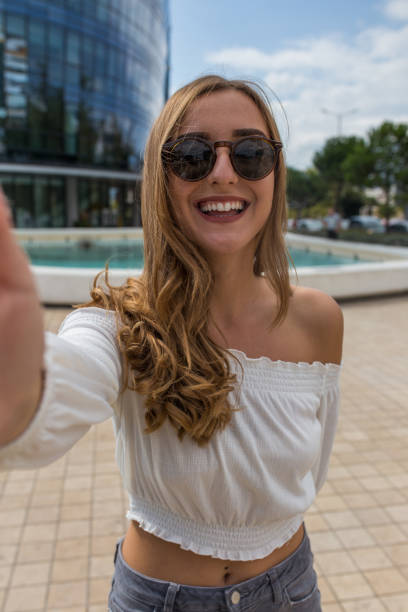 retrato de una joven chica milenaria atractiva tomando selfie con sus gafas de sol en y sonriendo a la cámara - autofoto fotos fotografías e imágenes de stock